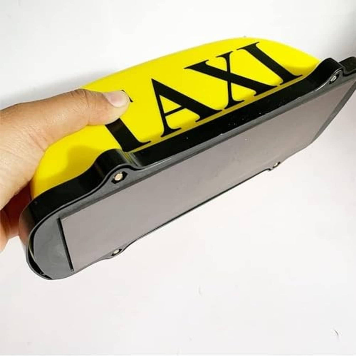 Yellow taxi roof light with black trim and TAXI letters, held in hand