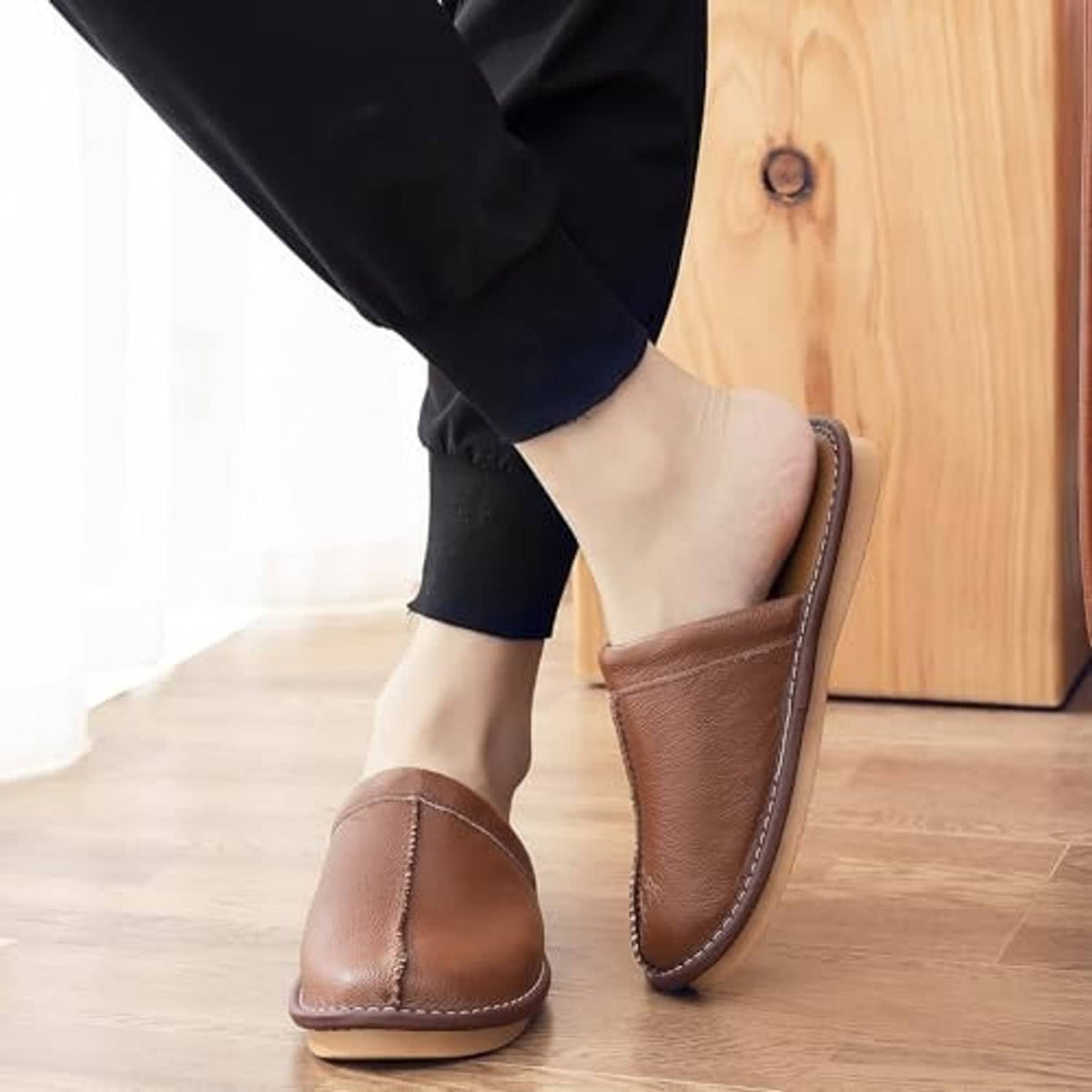 Light brown leather slippers on feet with rubber sole and contrast stitching