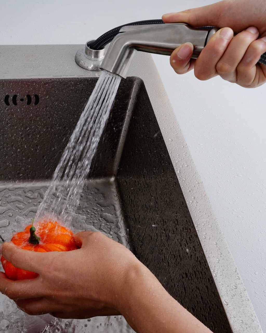 Hand using a brushed nickel sink sprayer attachment to rinse dishes at the faucet