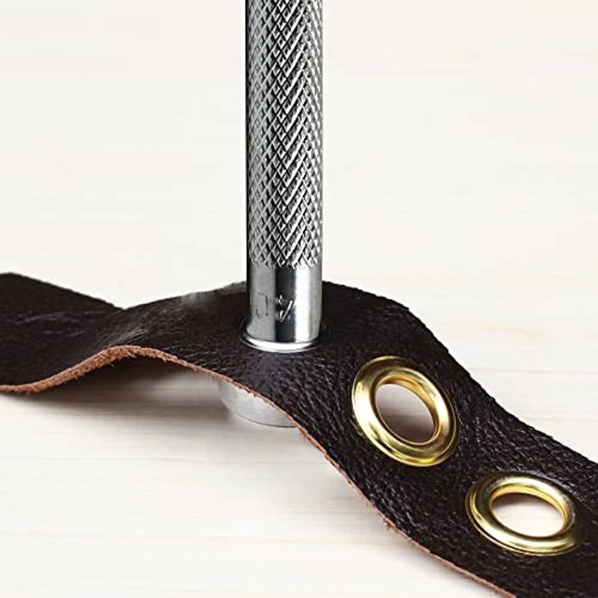 Metal grommet eyelet set into dark leather with silver setting tool