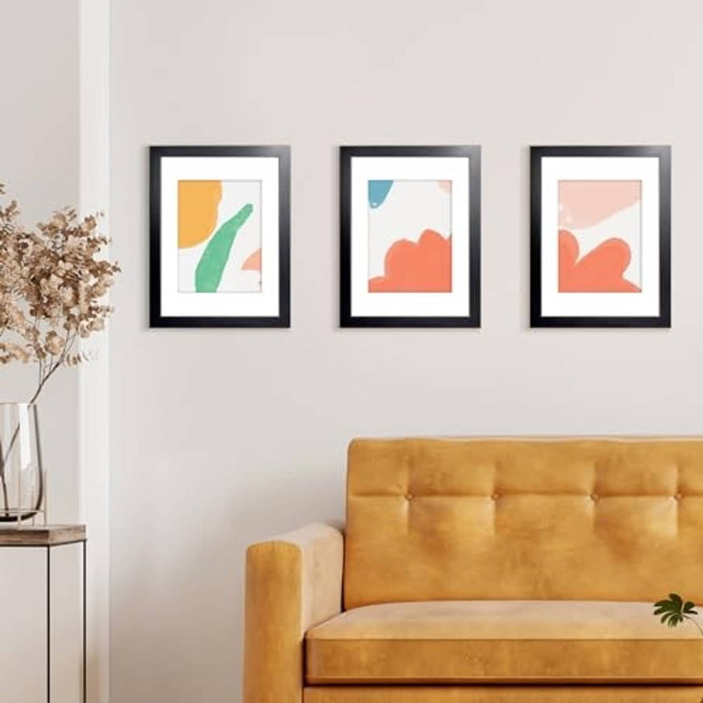 Set of three small black picture frames on a wall above a mustard-colored sofa