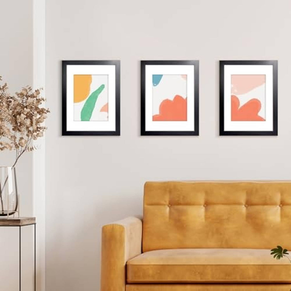 Set of three small black picture frames on a wall above a mustard-colored sofa