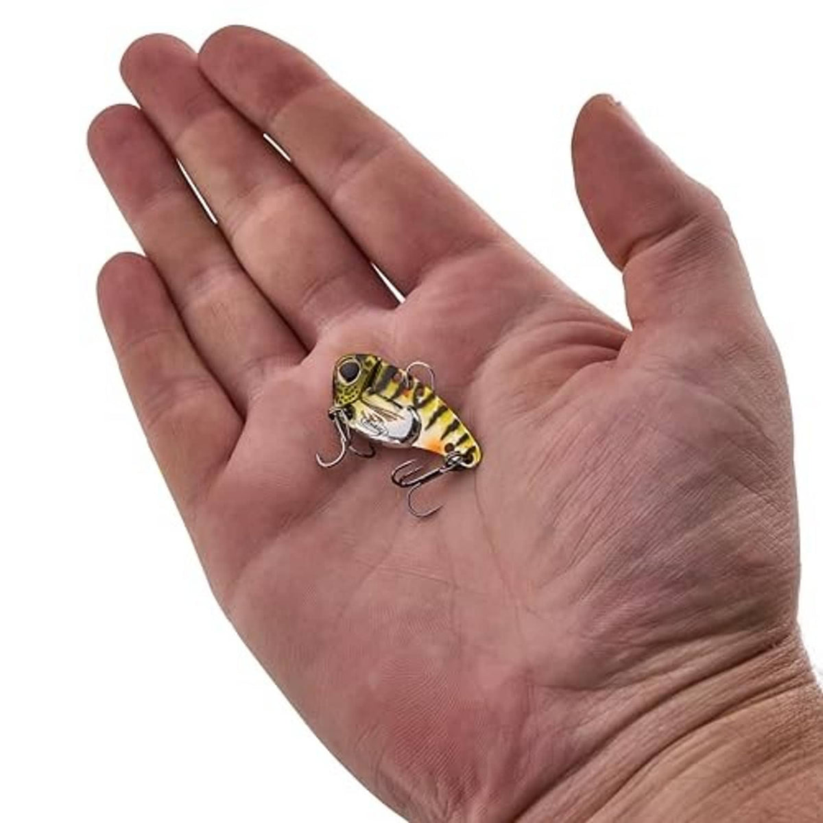 Blade bait lure held in palm, yellow-green patterned body with two treble hooks