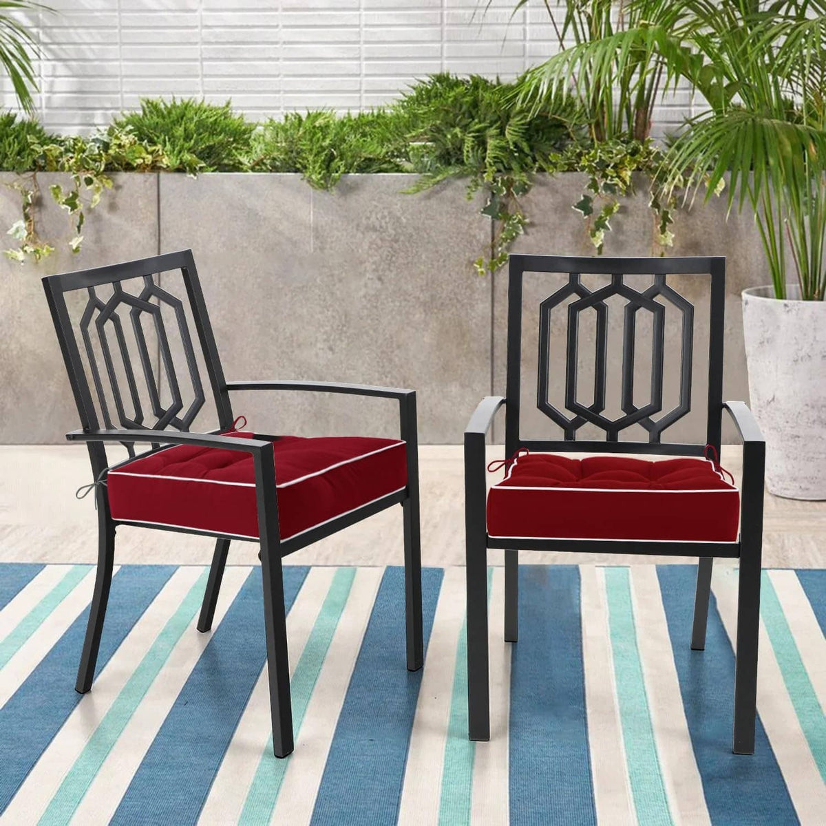 Two red tufted patio chair cushions with white piping and tie straps on black chairs