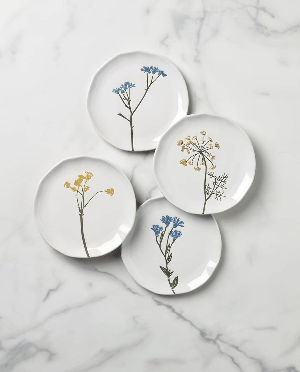 Four small wildflower plates with blue and gold botanical stems on white