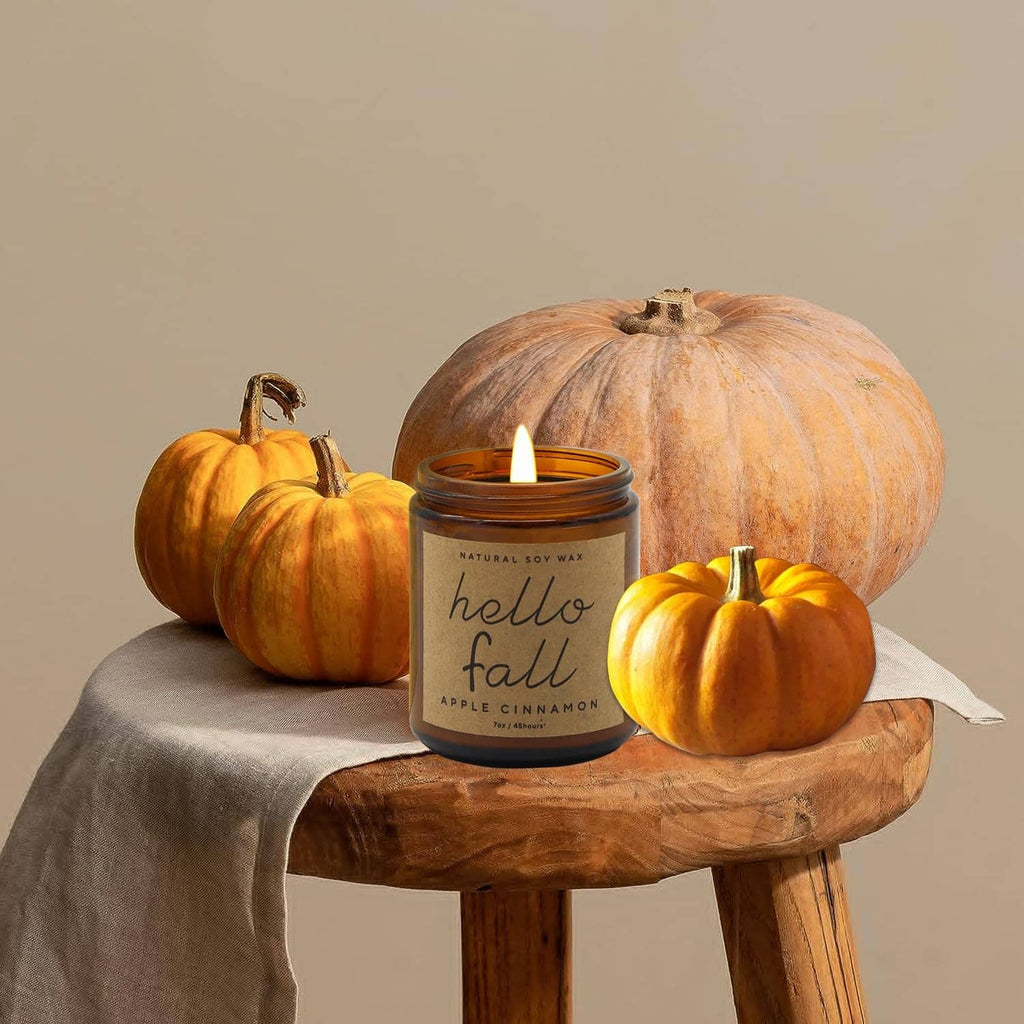 Hello Fall apple cinnamon soy candle in amber jar with white wick beside pumpkins