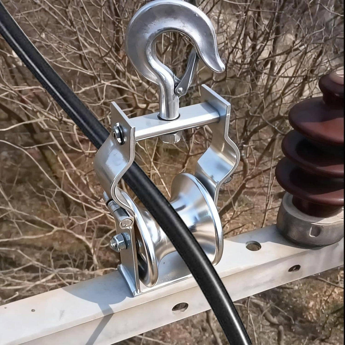 Cable pulley hook block clamped to a beam with black cable passing over the wheel