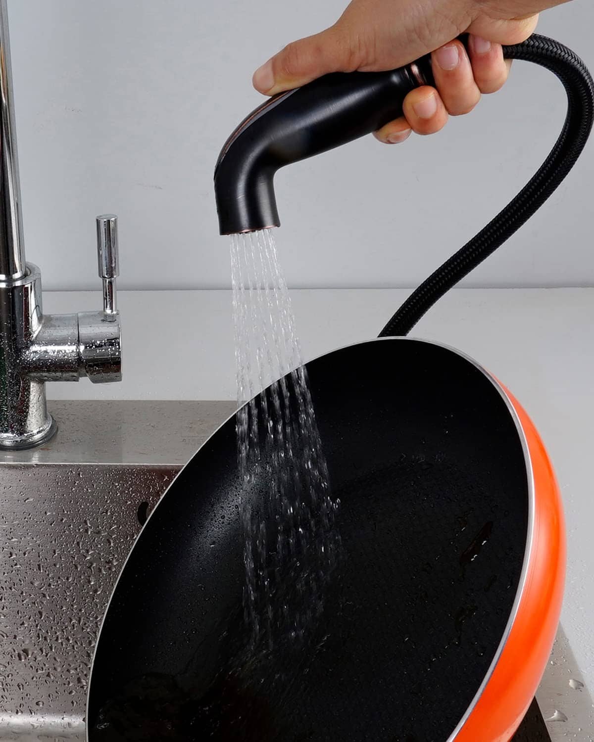 Black sink spray head releasing water from braided hose with bronze connection