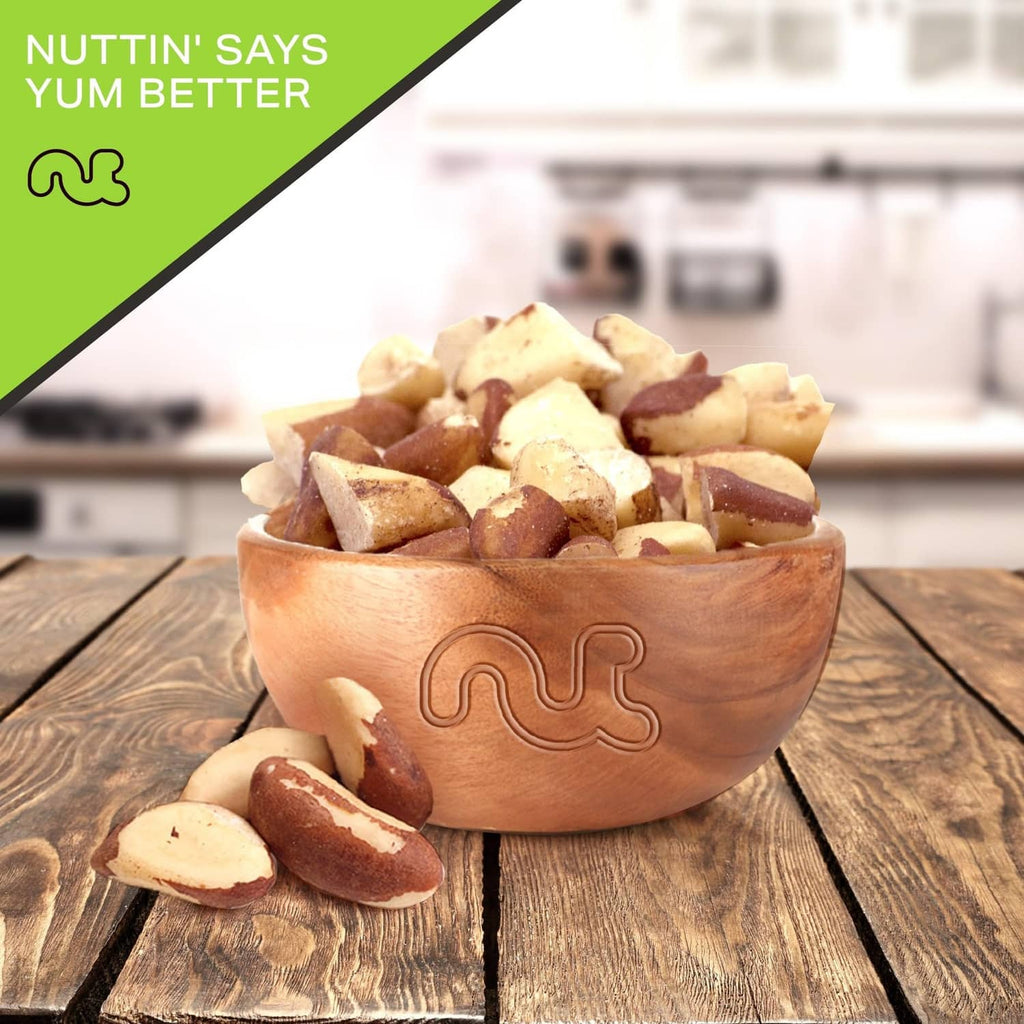 Wooden bowl filled with roasted salted broken Brazil nuts and a few pieces nearby