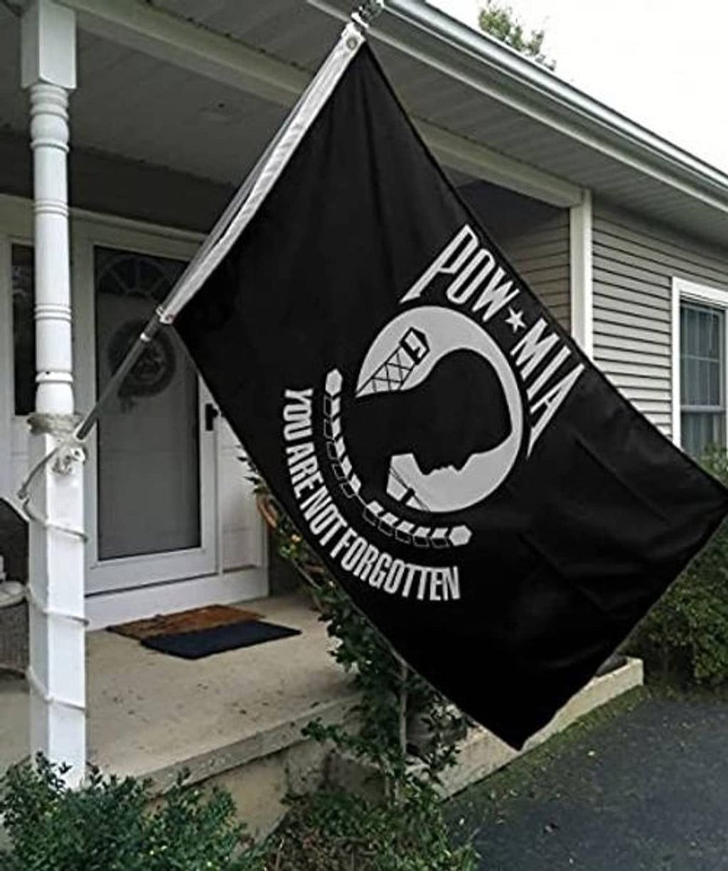 Black POW-MIA flag hanging outdoors on a pole with white embroidered emblem.