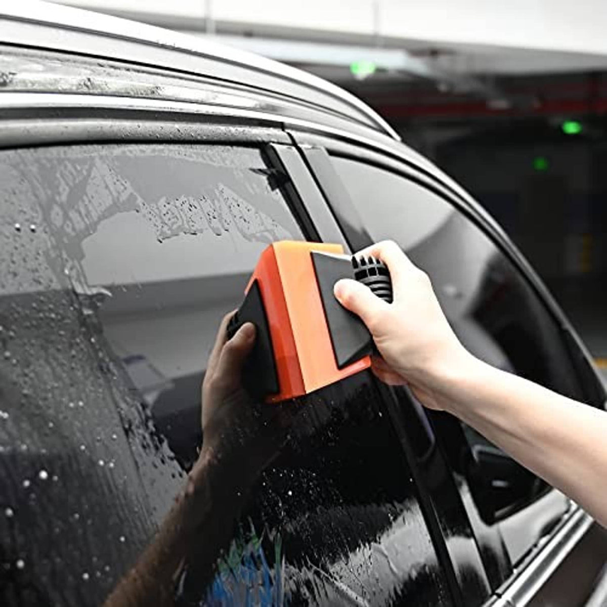 Hand holding orange-and-black window squeegee against car glass
