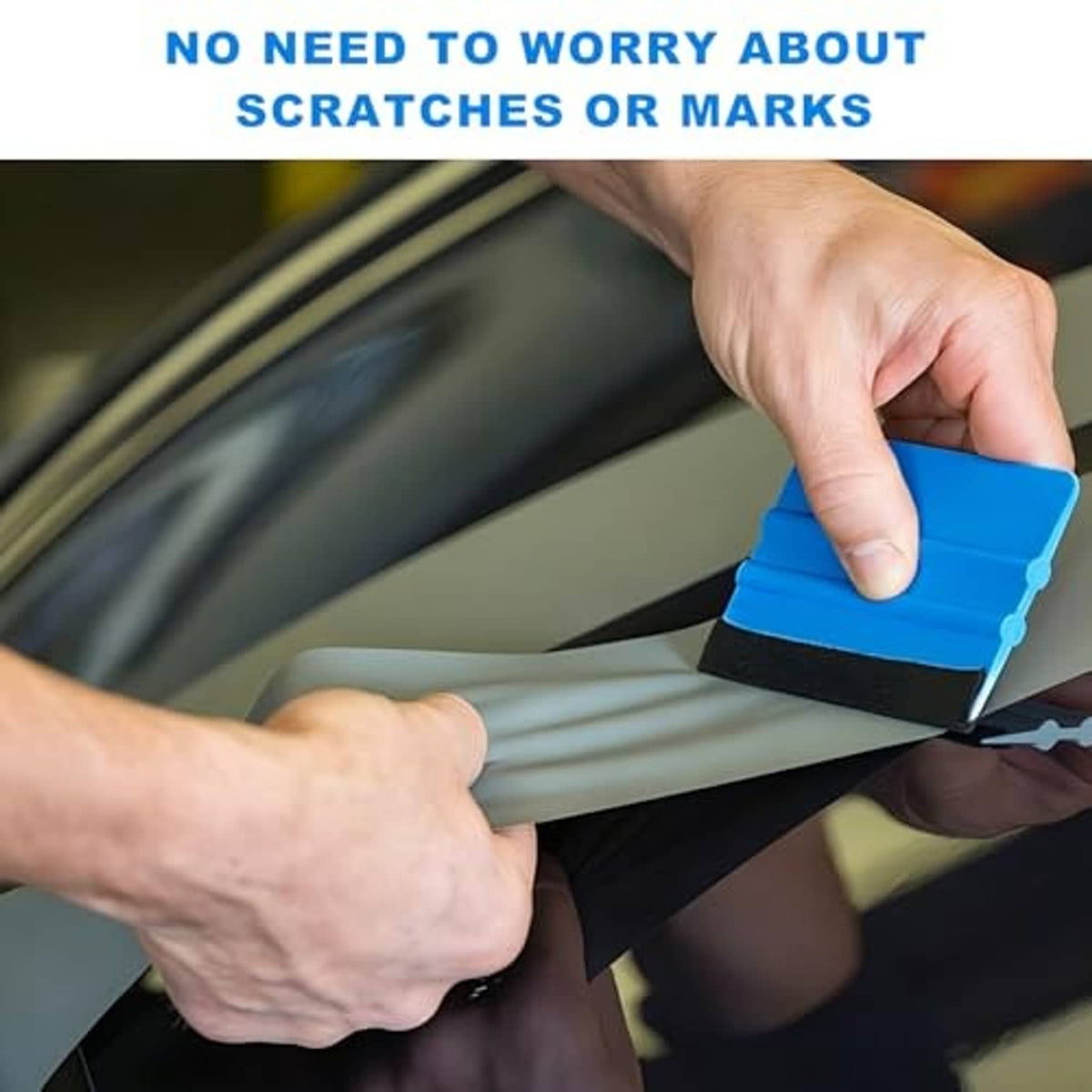 Hands using a blue plastic felt-edge squeegee to smooth window tint without marks