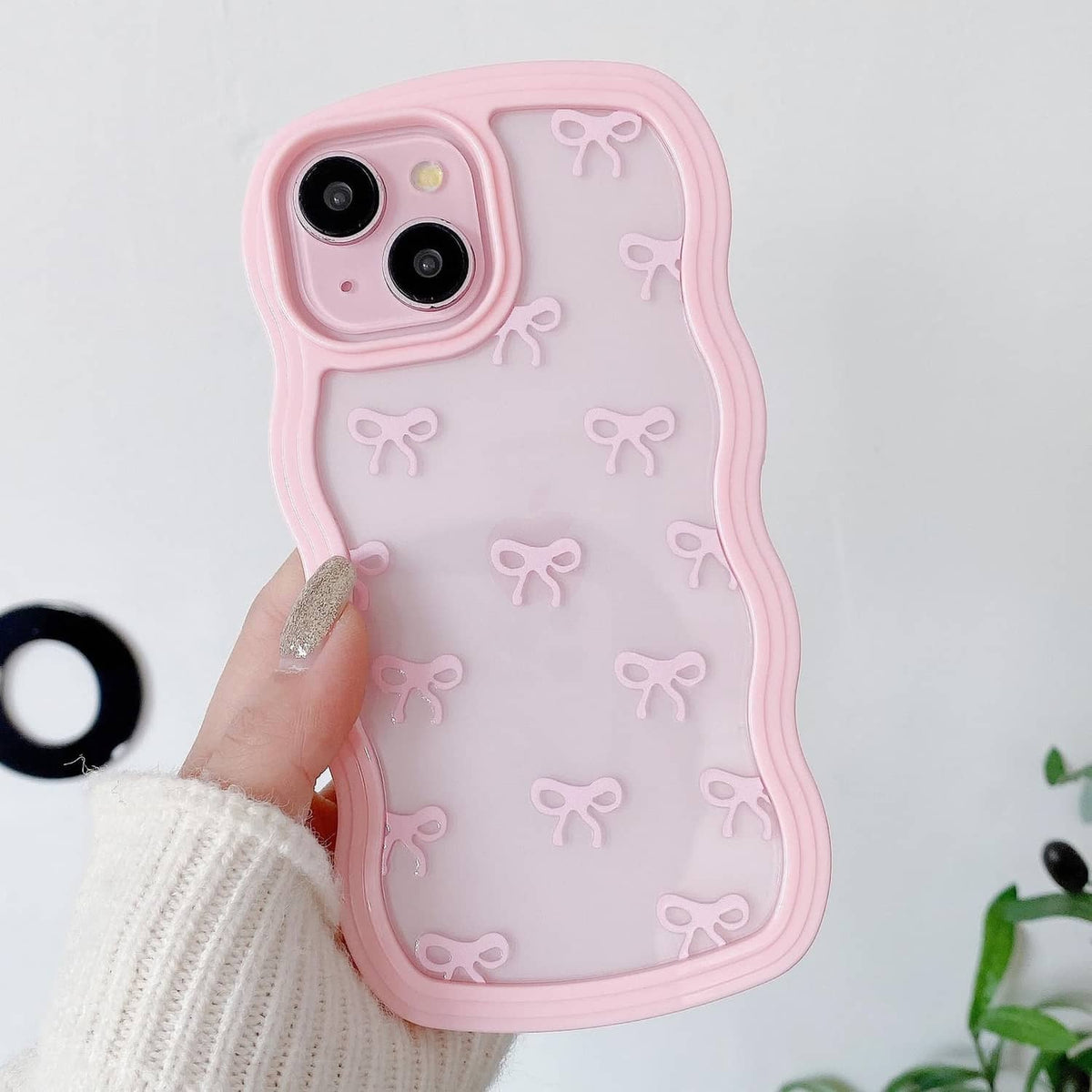 Pink clear iPhone case with repeating bow pattern and raised dual camera cutouts.