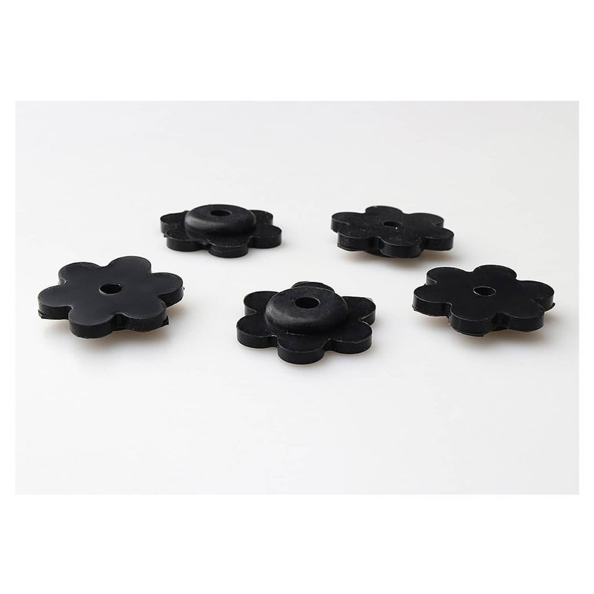 Five black flower-shaped rubber flag stops with center holes, spaced on a flat surface
