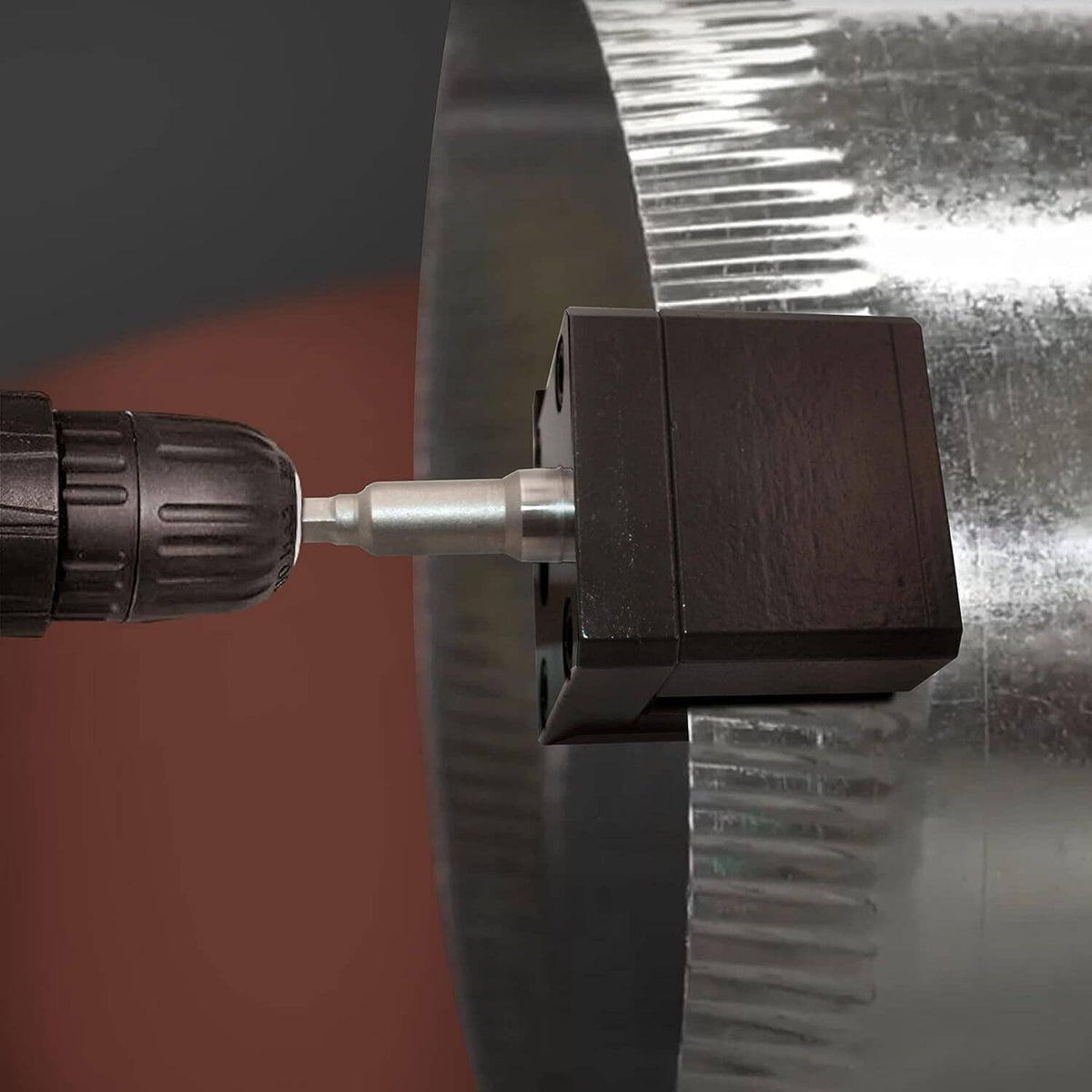 Black crimper block contacting metal sheet with steel driver shaft from drill