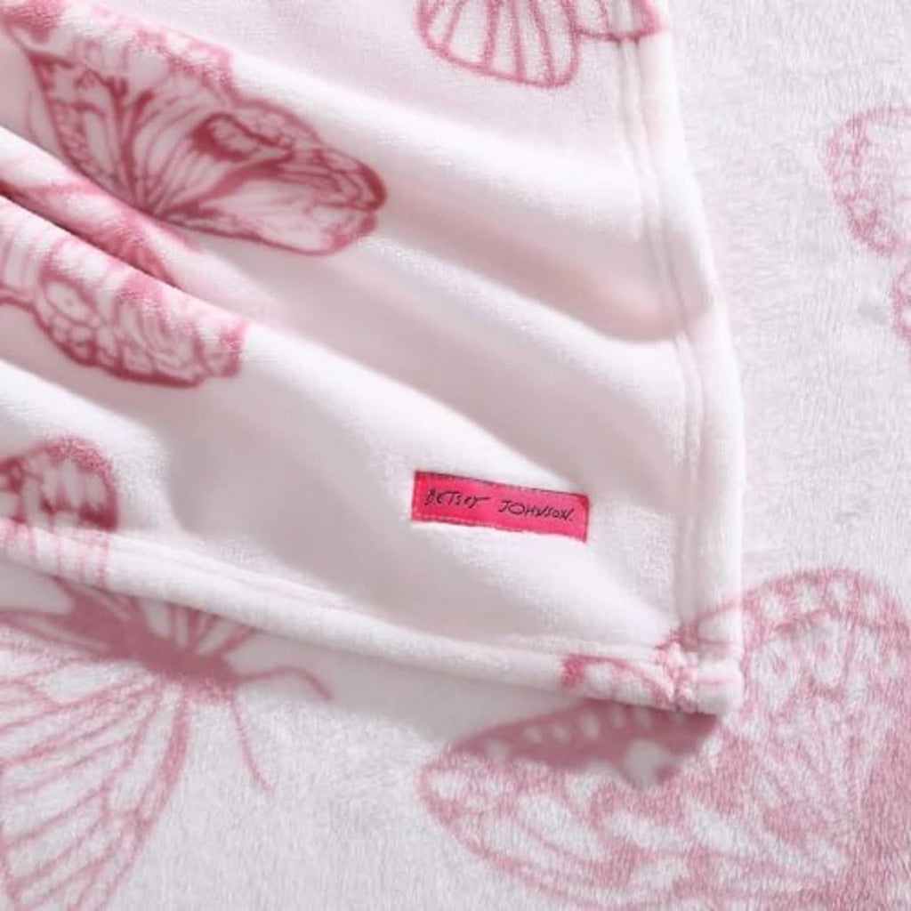 Pink butterfly-print blanket close-up with stitched hem and logo patch