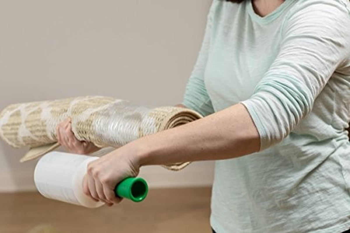 Person applying Duck Brand stretch wrap roll around rolled items with green dispenser