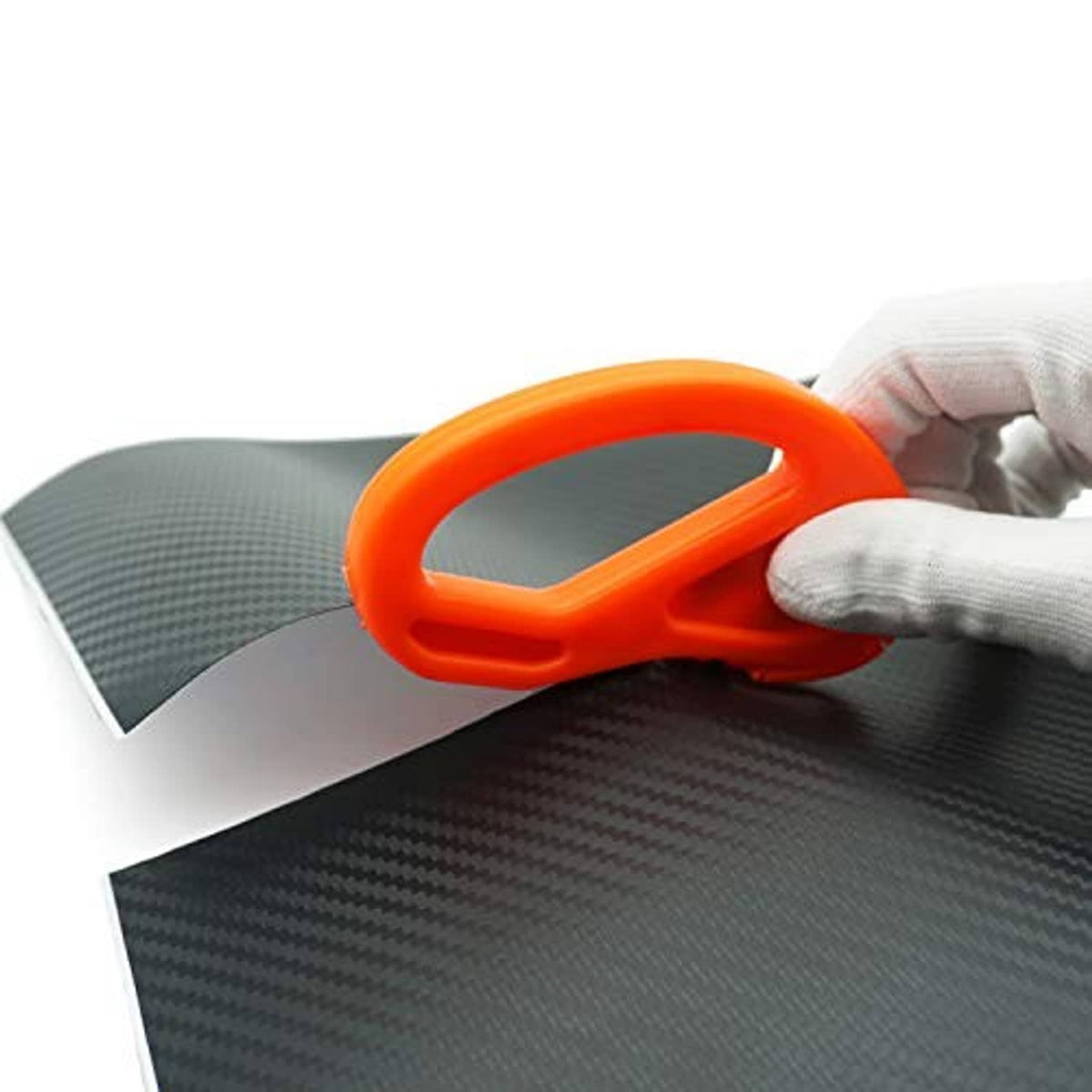 Orange plastic vinyl scraper held by a gloved hand on dark carbon-fiber film