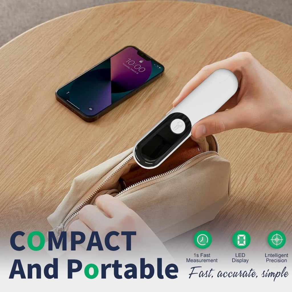 Compact white non-contact forehead thermometer in hand next to a zipper pouch and smartphone