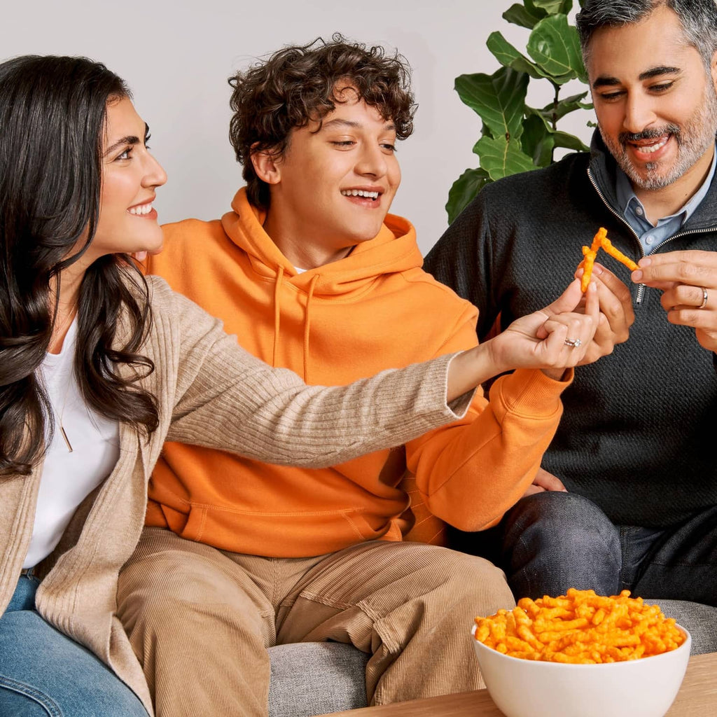 Crunchy orange cheese snack chips in bowl and held in hand at home
