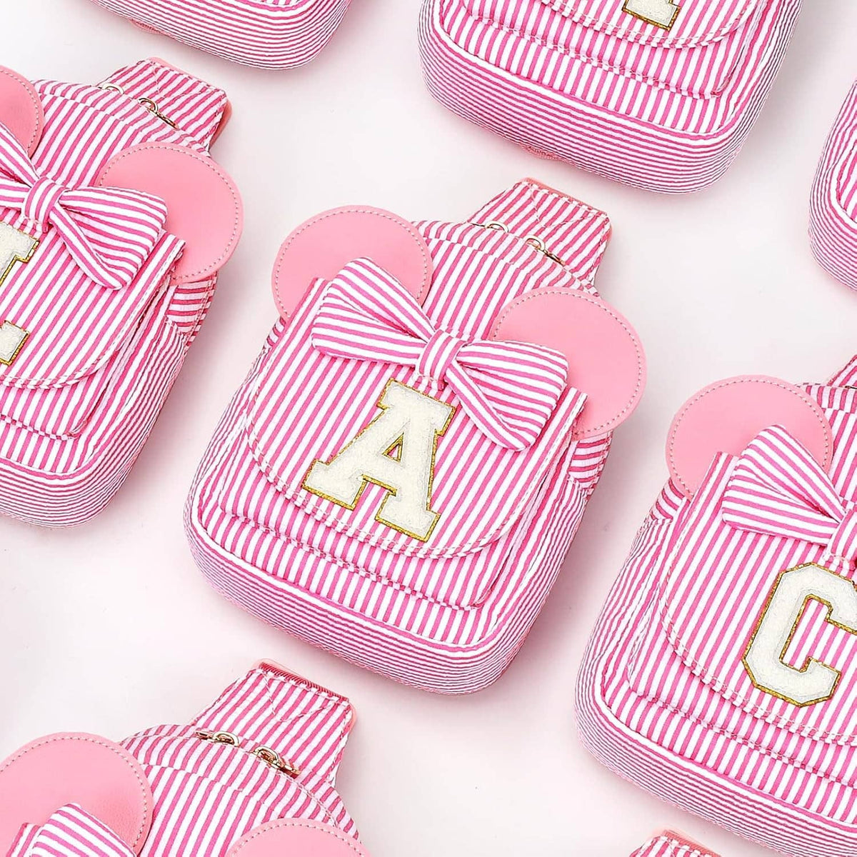 Assorted pink striped sling bags with bow fronts and letter patches