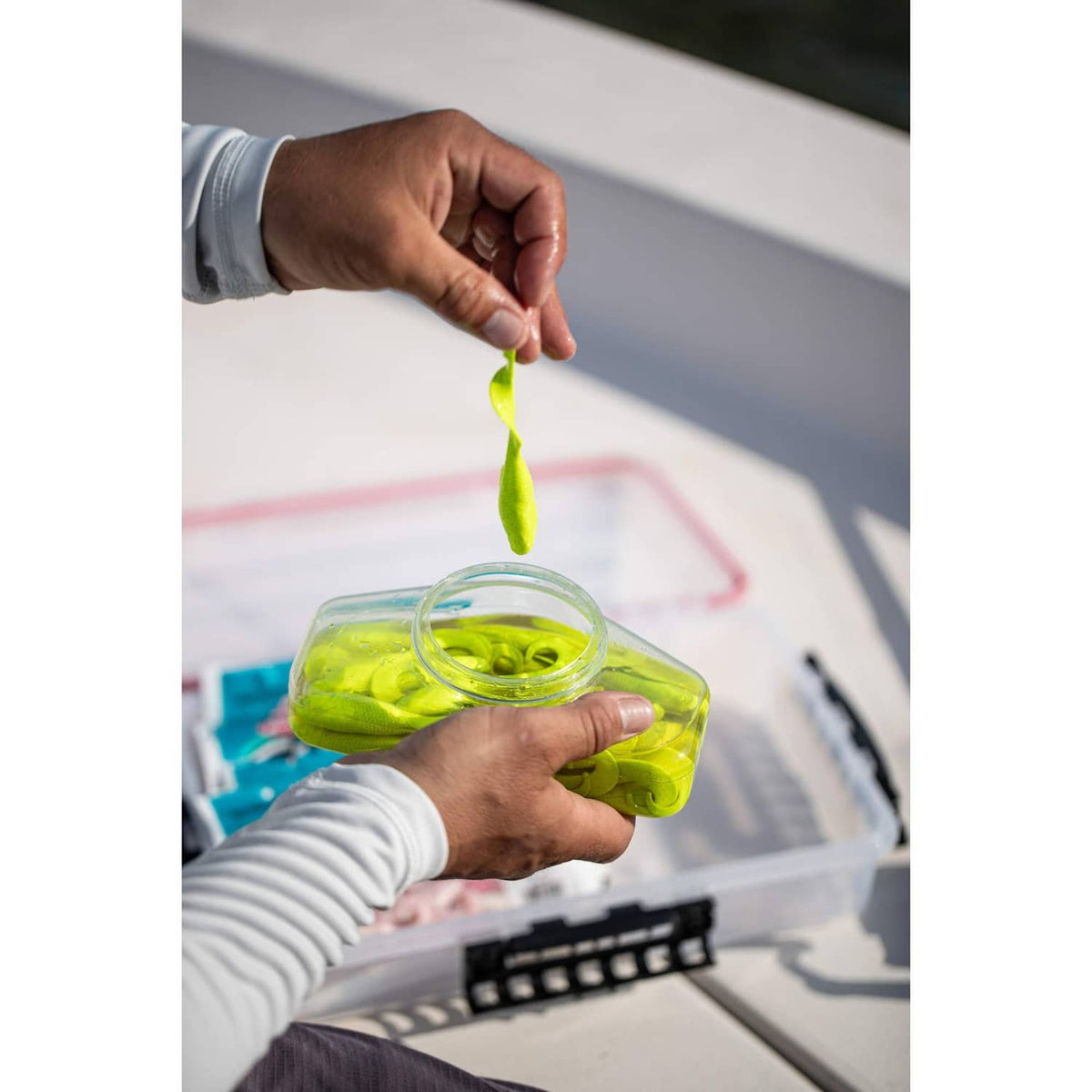 Green soft fishing bait lure hanging above a translucent bait container