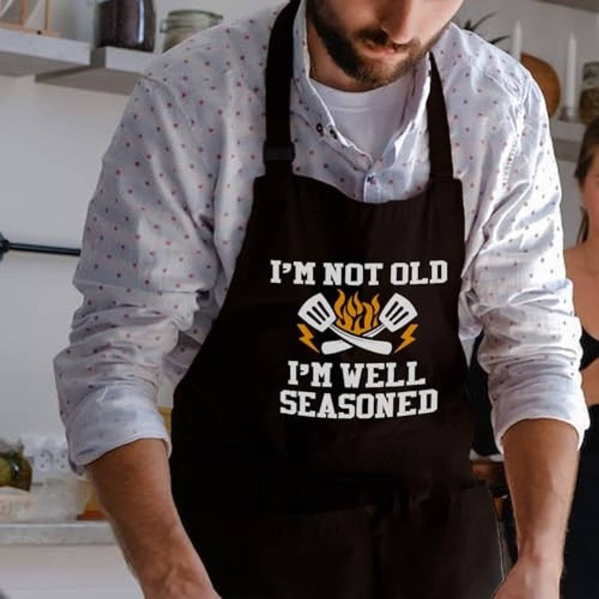 Men's black apron worn over a light shirt with 'I'm well seasoned' front print