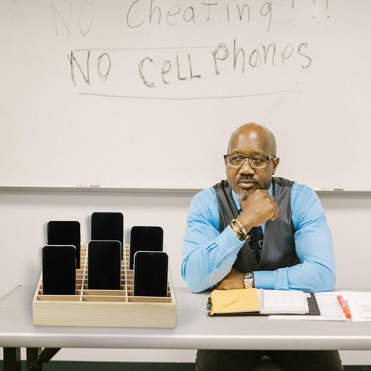Wood cell phone organizer tray with multiple phones standing upright in classroom