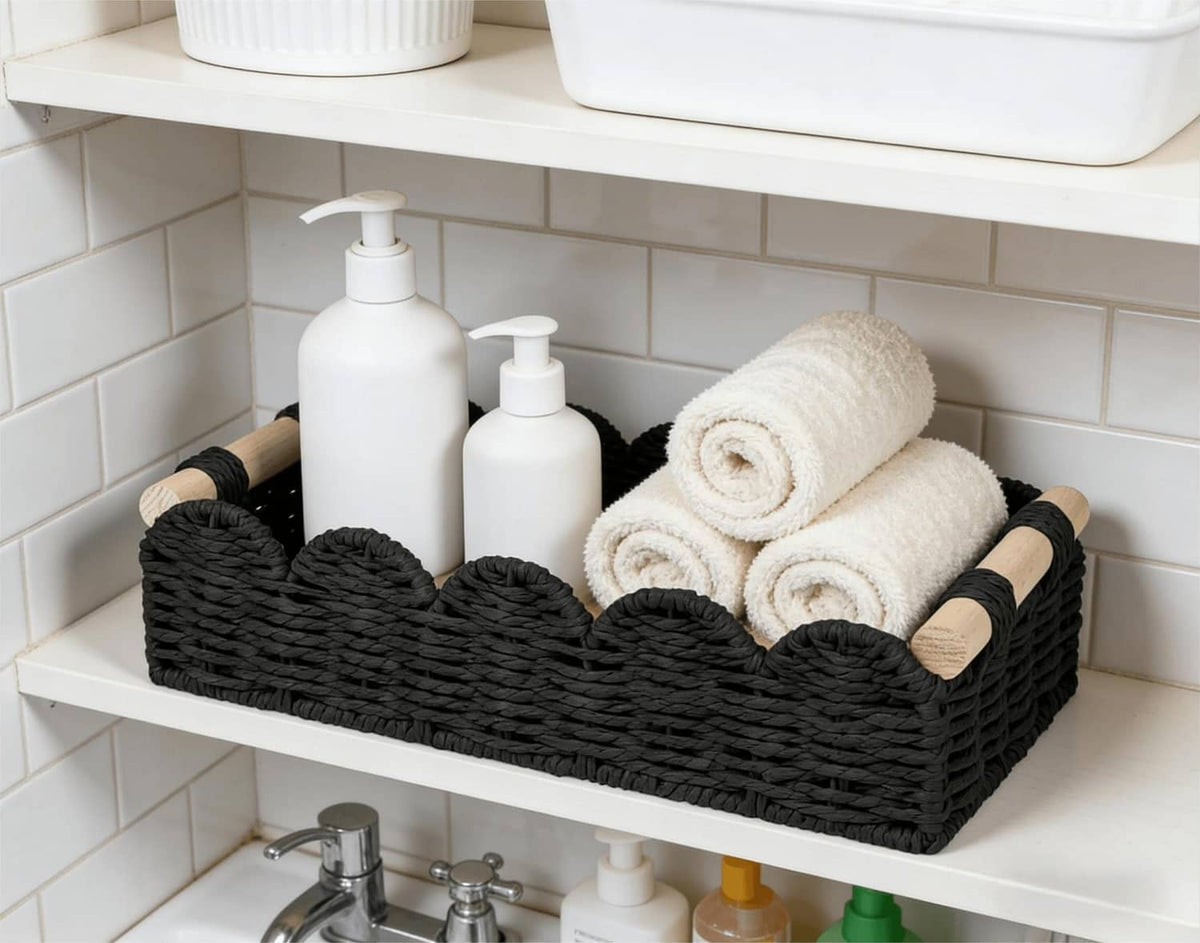 Black woven storage basket with wood-capped handles holding bottles and folded towels