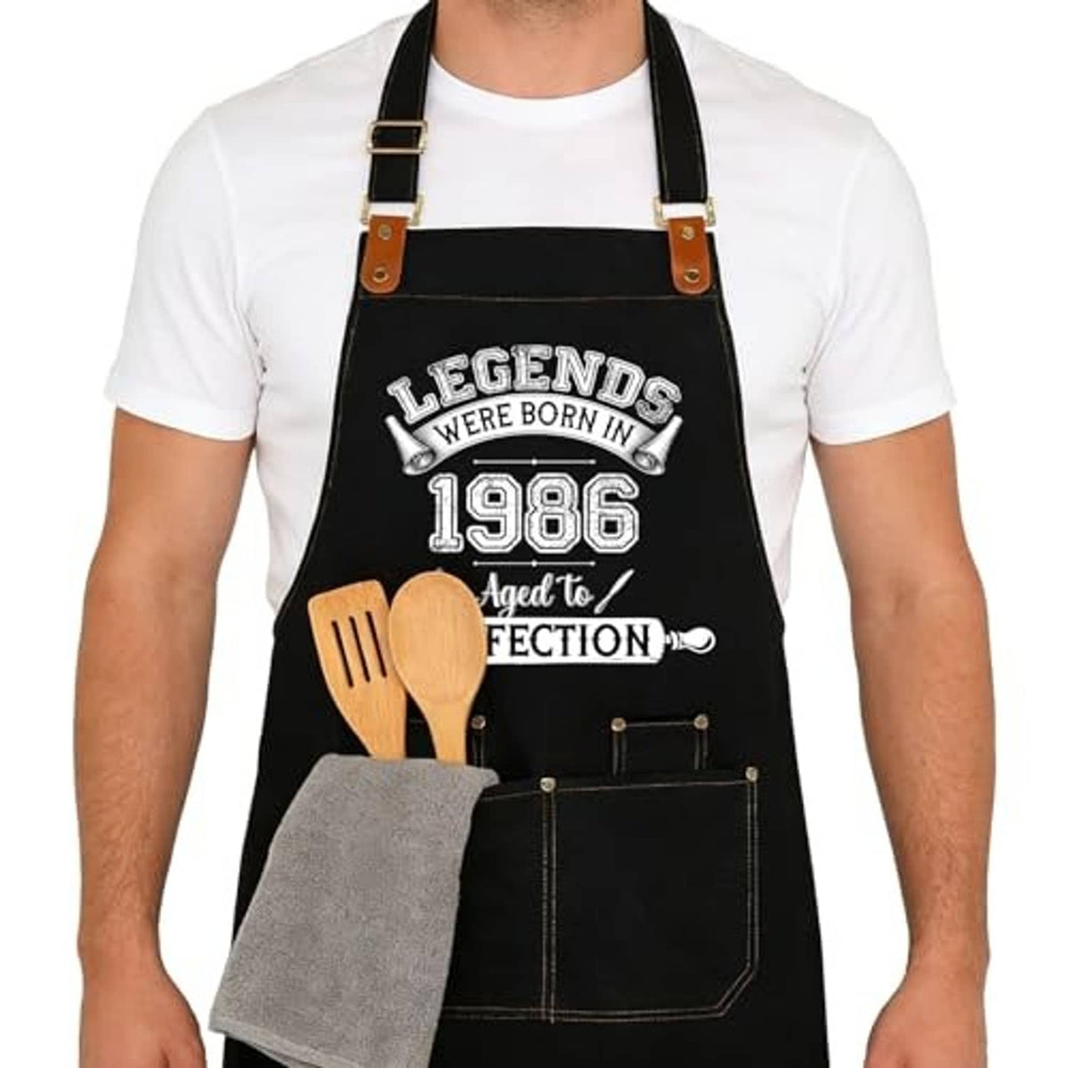 Black cooking apron with printed 1986 design and front pockets, worn by a man.