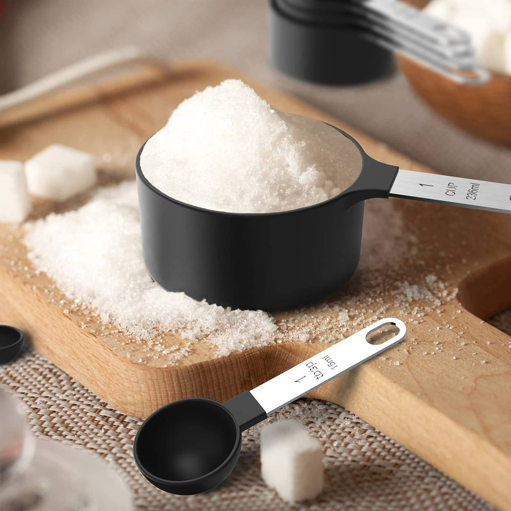 Black measuring cup filled with sugar crystals and a matching measuring spoon on wood