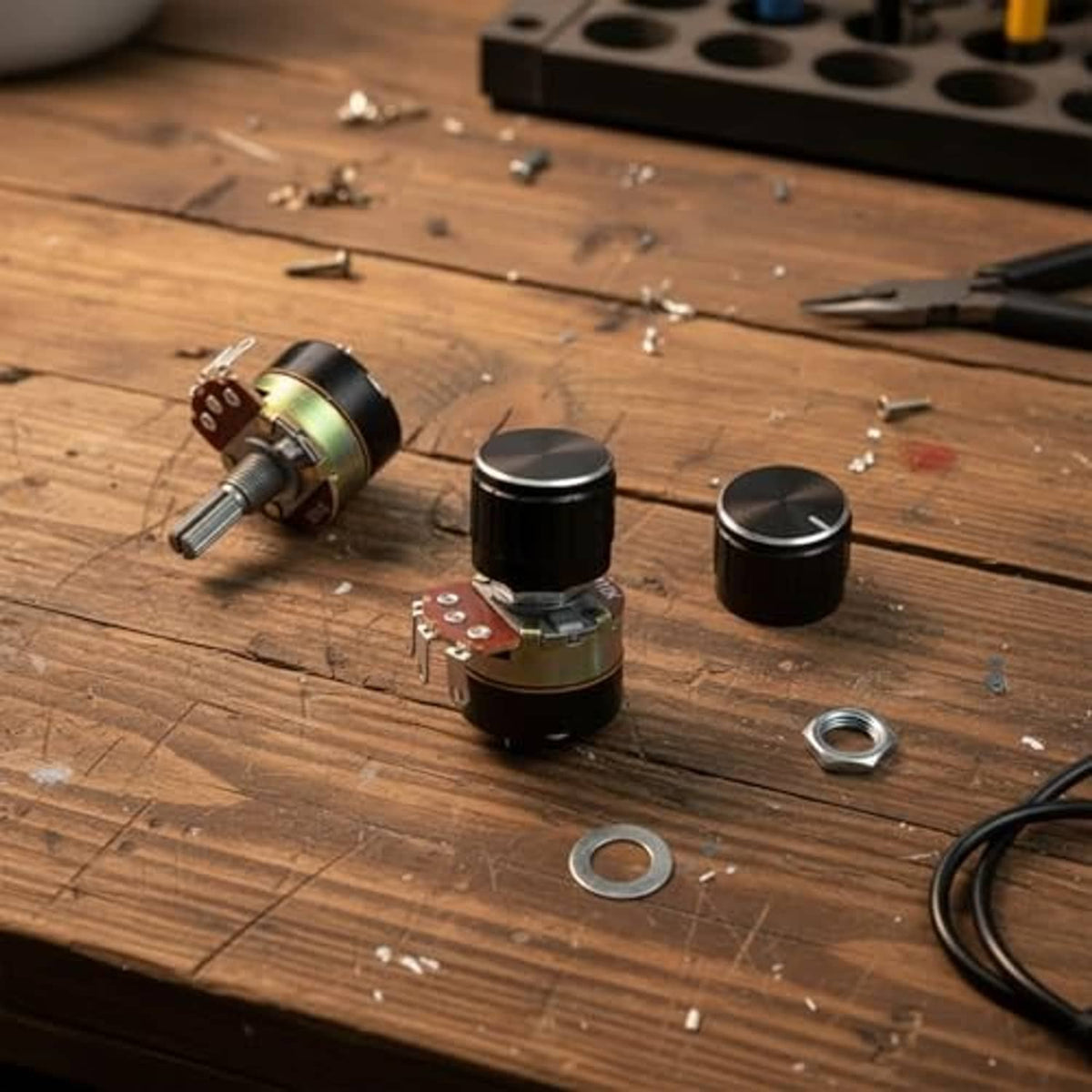 Two black potentiometers on a workbench with nuts, washers, and wire leads
