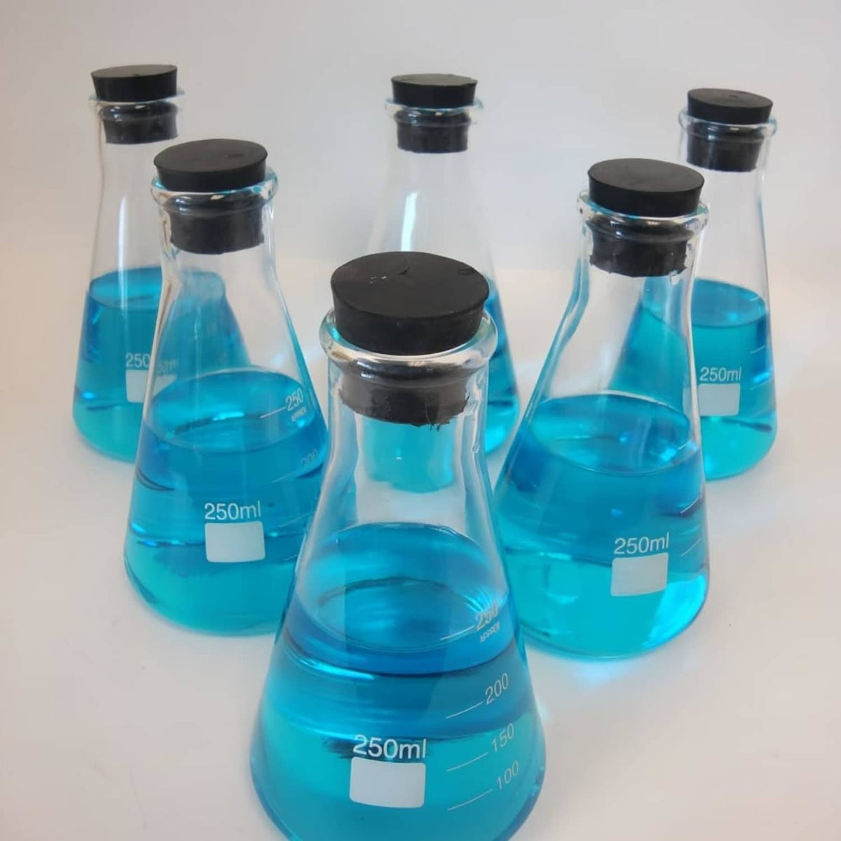 Multiple blue glass lab flasks with black rubber stoppers on top