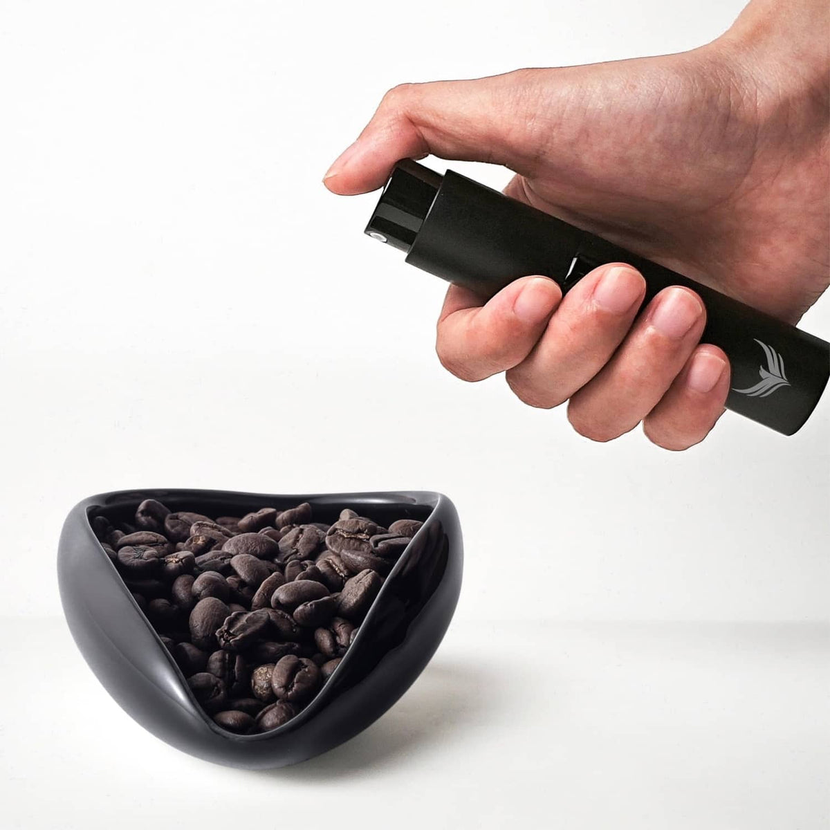 Black coffee dosing cup and RDT sprayer held above a cup of coffee beans