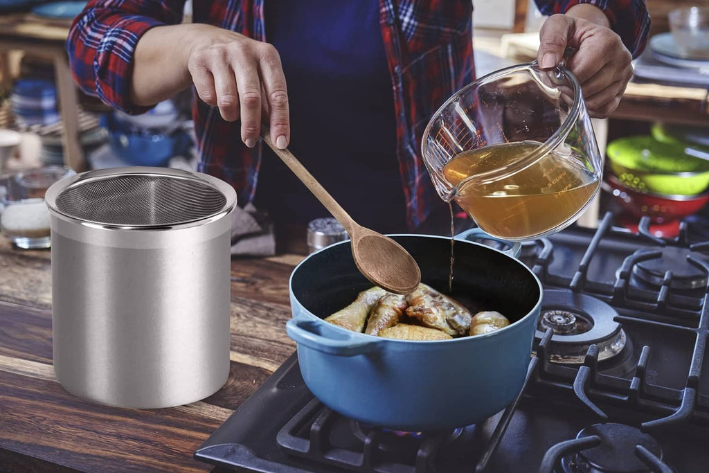 Stainless steel oil storage container with fine mesh strainer beside a frying pan