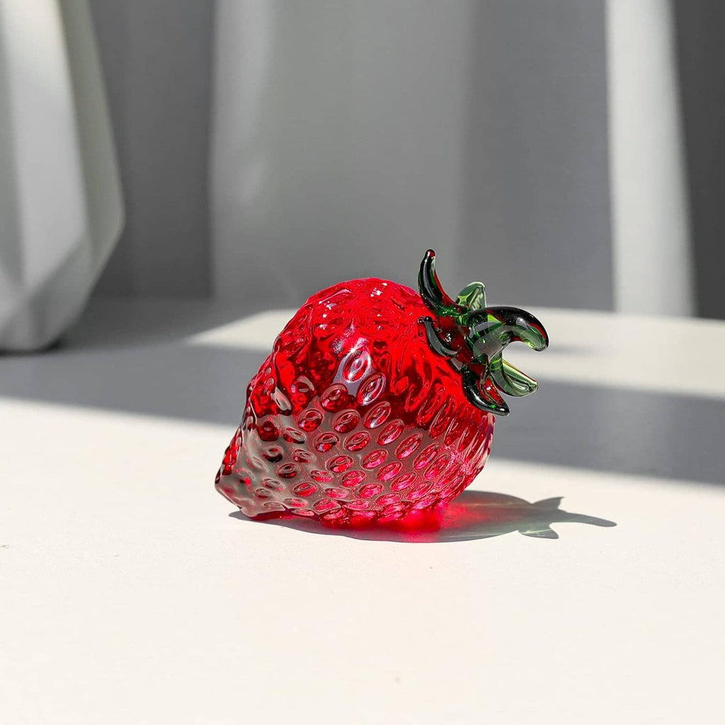 Red glass strawberry paperweight figurine with raised green leaves on tabletop