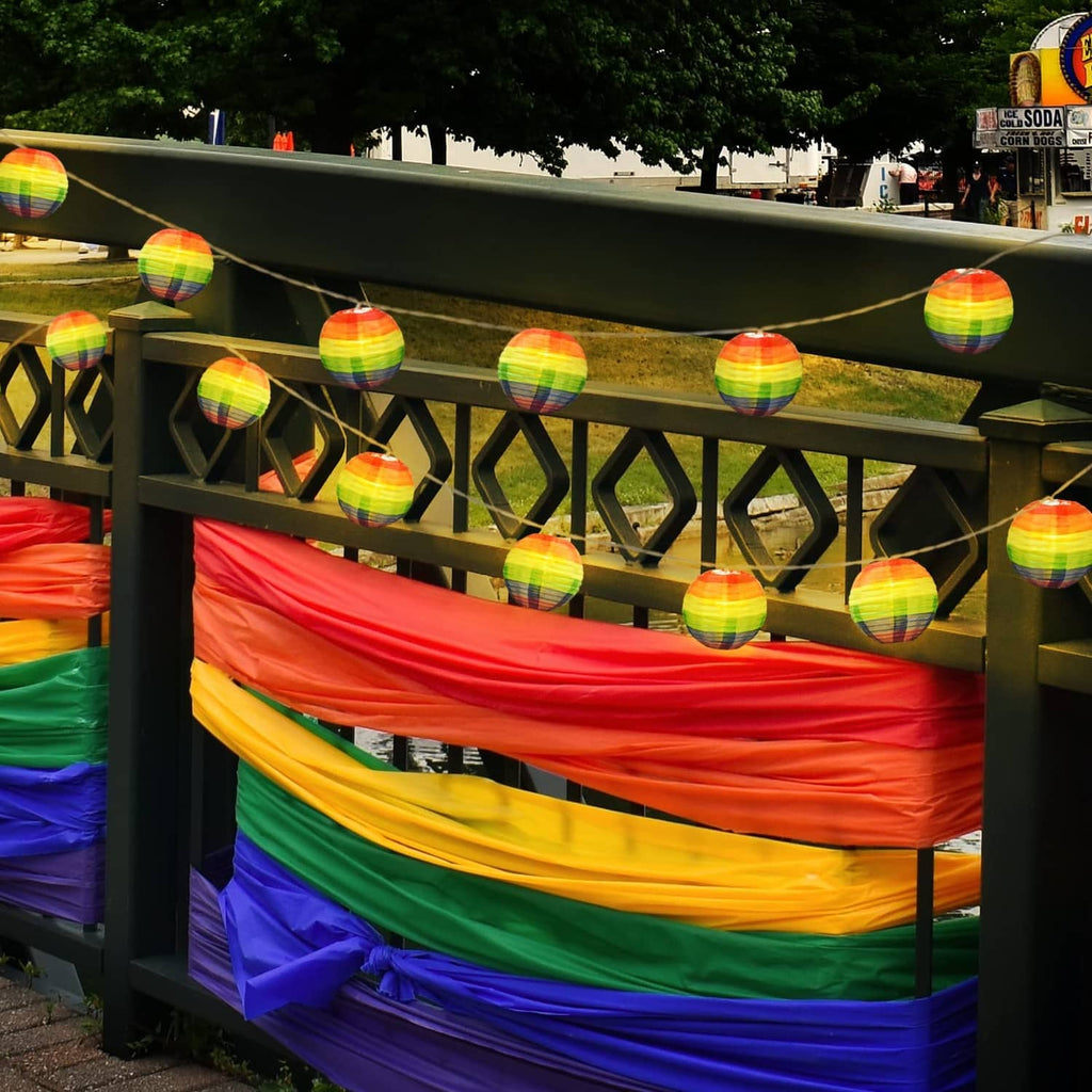 Hanging rainbow lantern string lights with striped nylon globes outdoors on railing
