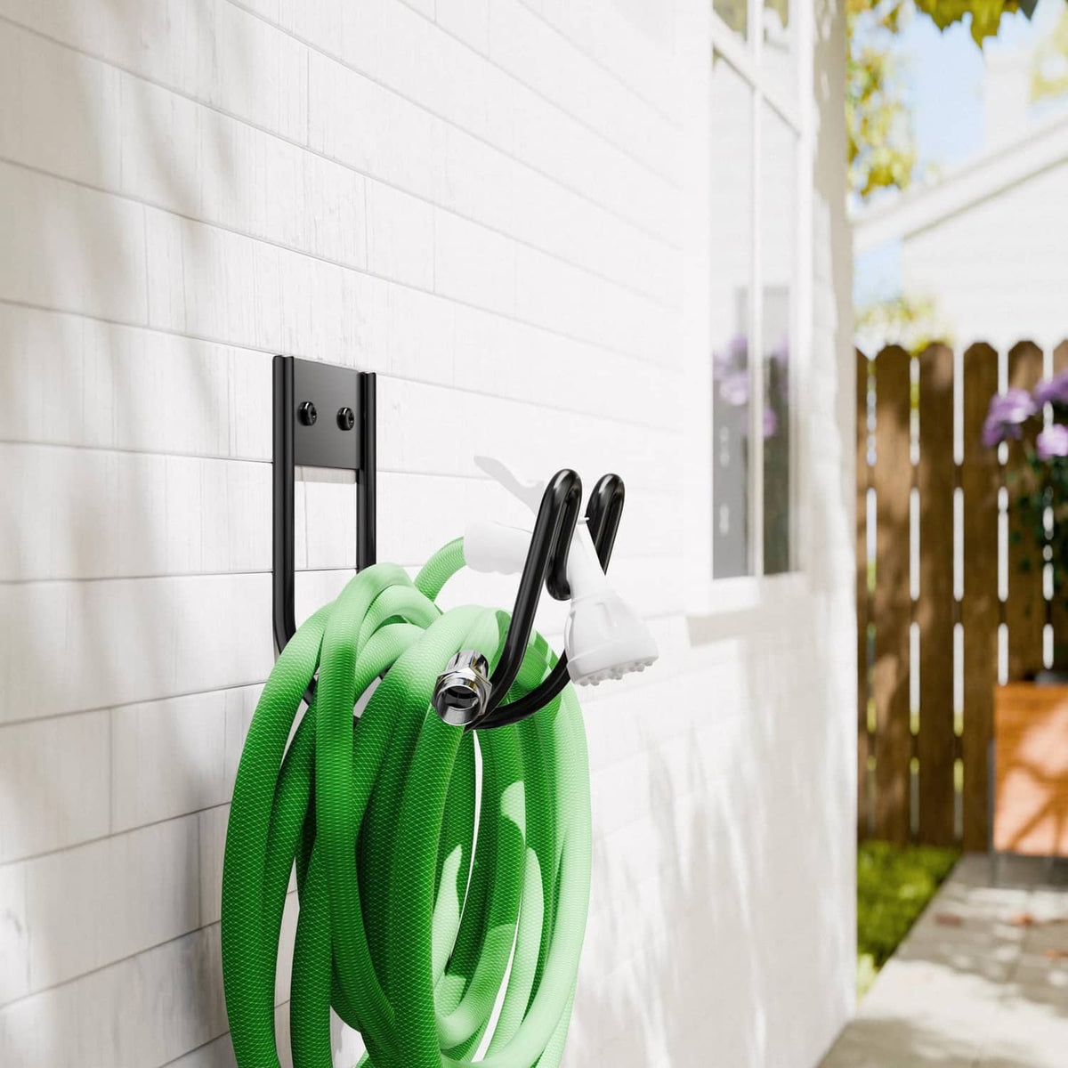 Black metal hose holder plate on wall with two curved hooks and wrapped green hose