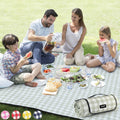 Green and white check picnic blanket with roll-up carry pouch on grass.