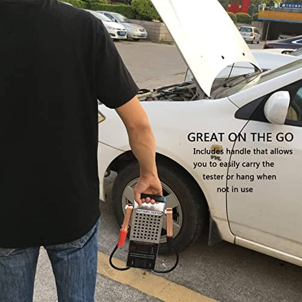 Battery load tester being carried beside a car, with red and black clamp cables