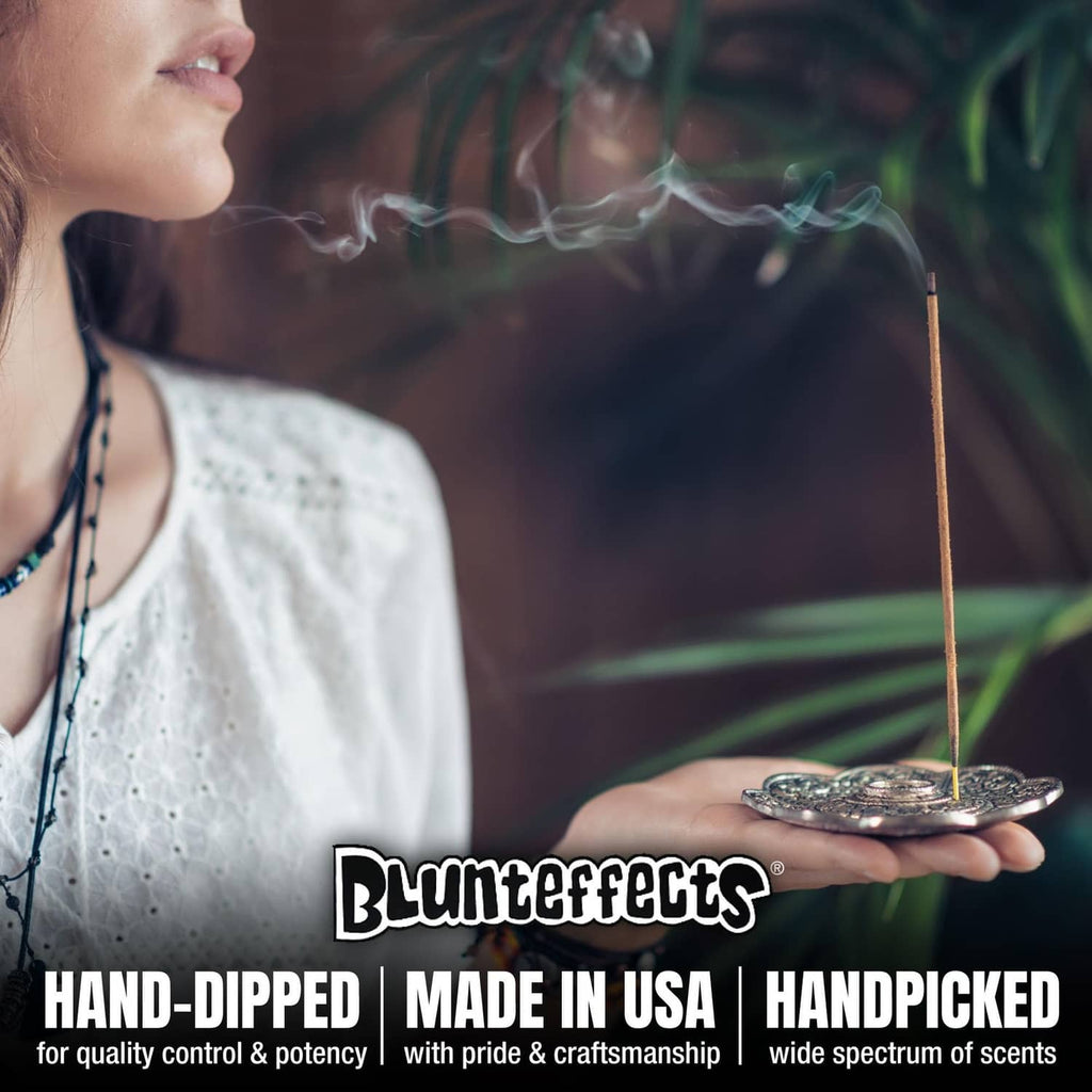 Hand holding hand-dipped incense sticks above a metal incense holder tray