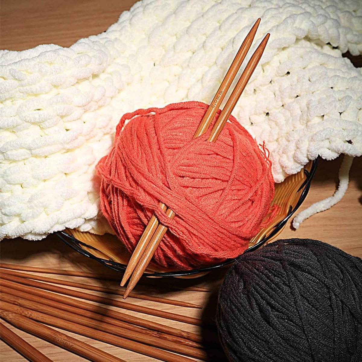 Double-pointed bamboo needles resting on yarn balls and knitted blanket