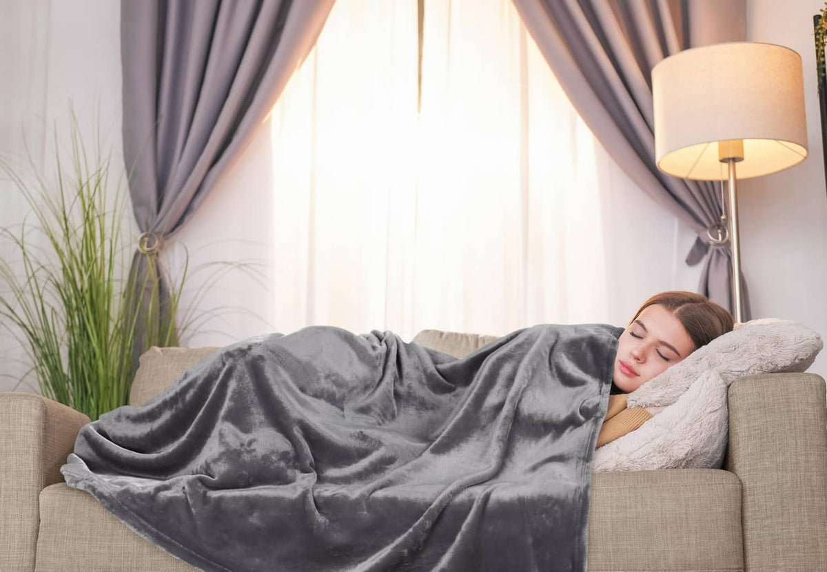 Grey fleece blanket spread on a couch while a person relaxes under it.