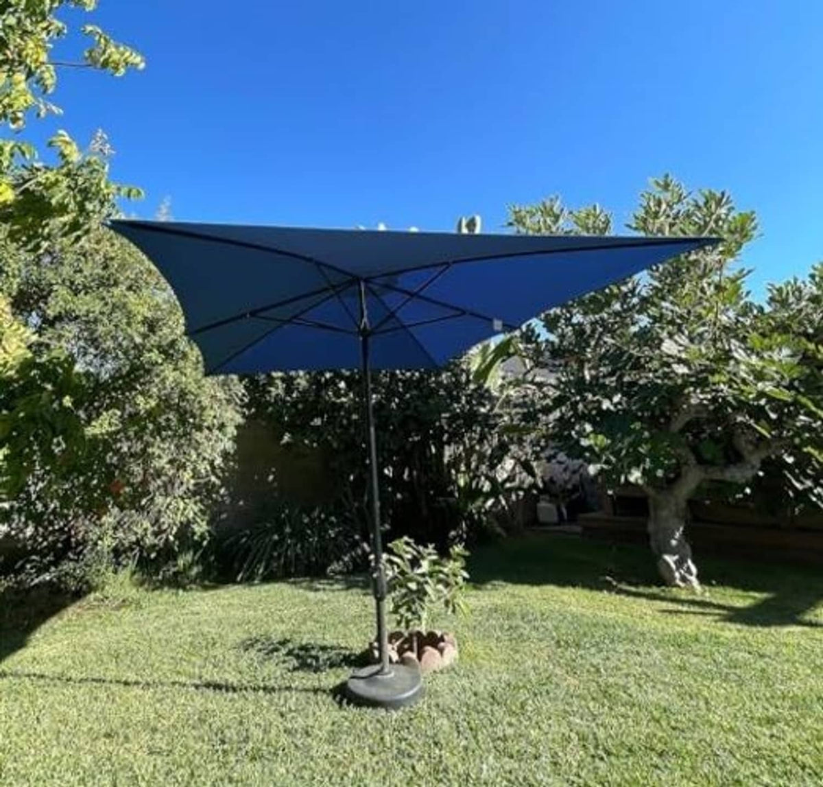 Blue rectangular umbrella canopy on black stand, fully spread above green grass.