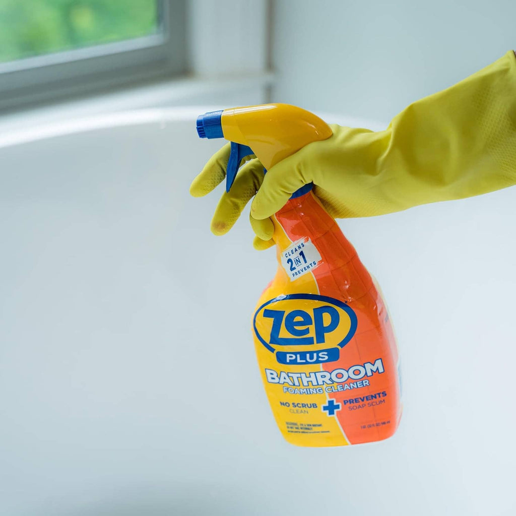 Hand spraying Zep Plus Bathroom foaming cleaner bottle with blue trigger, yellow-orange