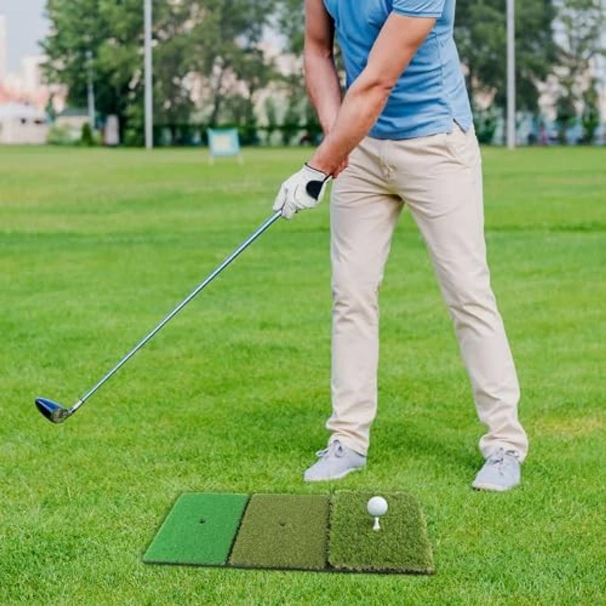 Portable golf hitting mat on grass with white practice ball and golfer preparing to swing.