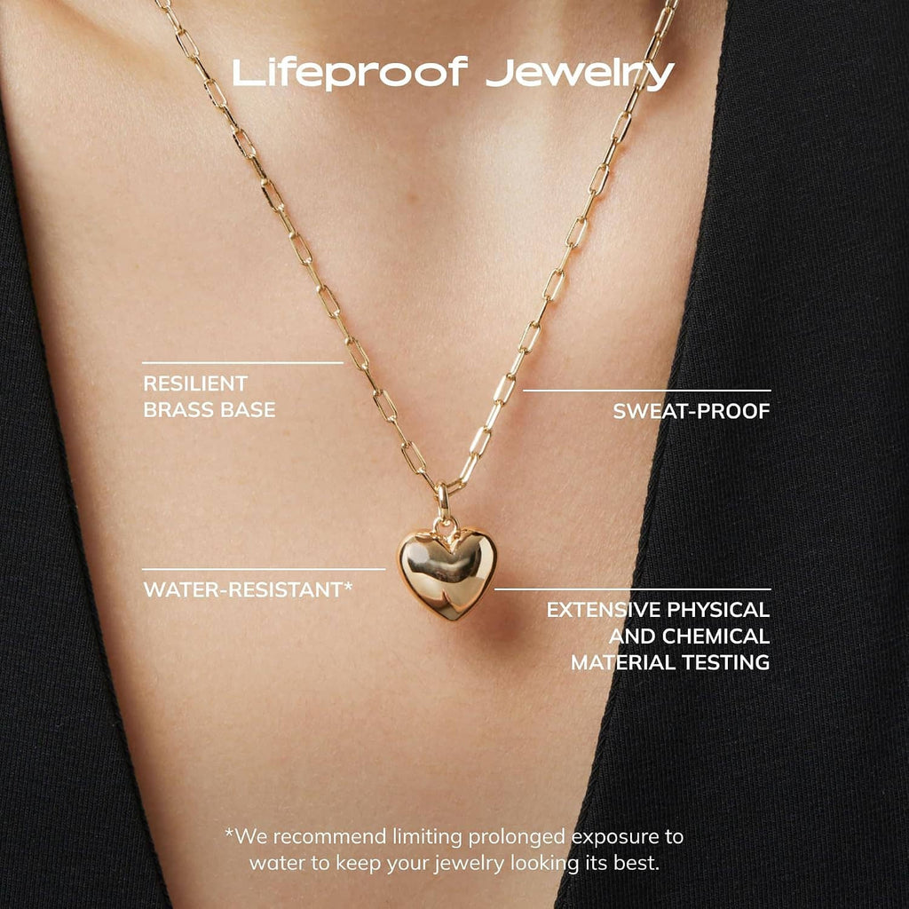 Gold heart pendant necklace with paperclip chain on neckline, close-up