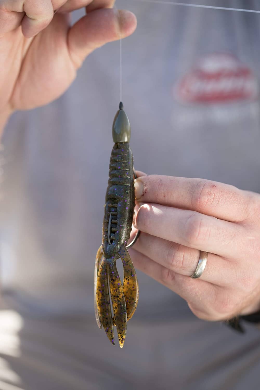 Green and gold speckled soft plastic lure in hand with pointed head