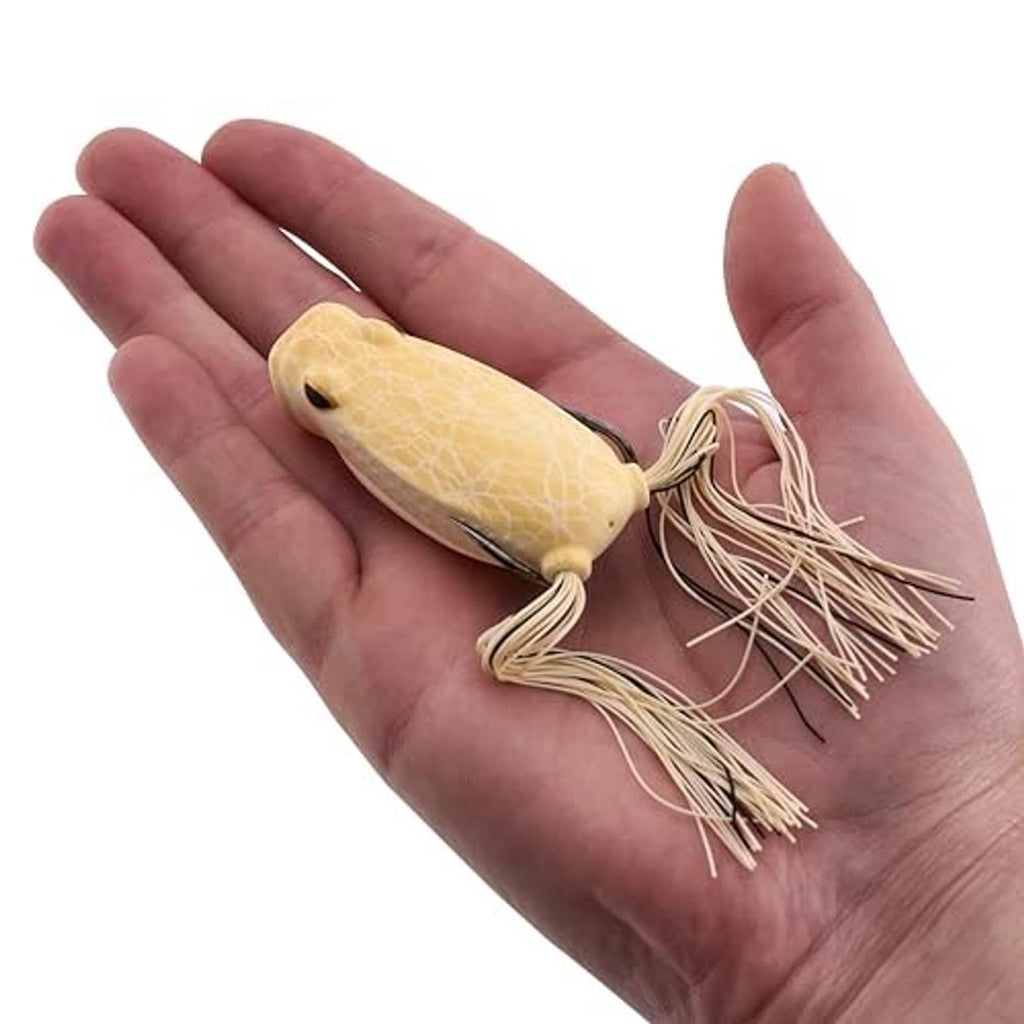 Tan soft frog lure in open palm, showing cream skirt and two barbed hooks