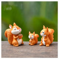Miniature squirrel figurines set of three, orange and white, standing on a wooden surface